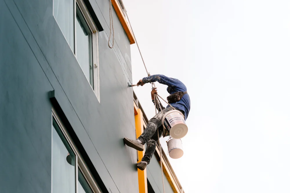 8287742e81 Commercial painter using rope access to paint a multi-story building exterior.